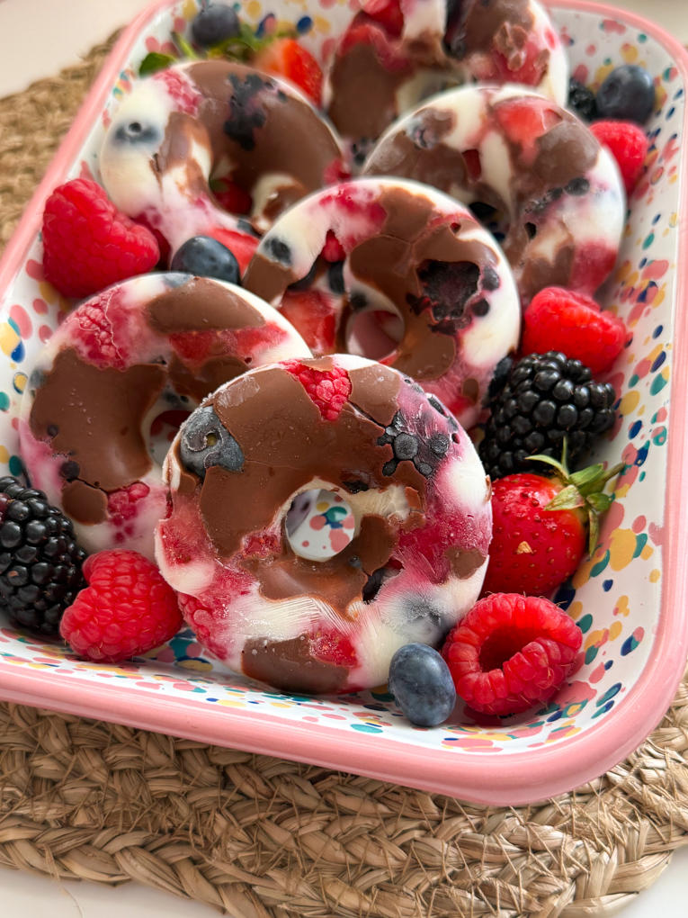 Six frozen yogurt berry donuts in a pink spot patterned rectangle dish and garnished with fresh berries.