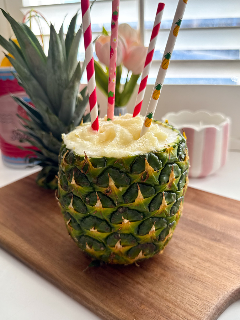 A fresh pineapple filled with slushie with four colourful straws in the top.