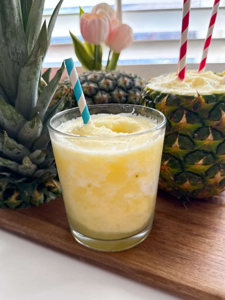 Pineapple slushie in a clear glass with a white and blue striped straw.