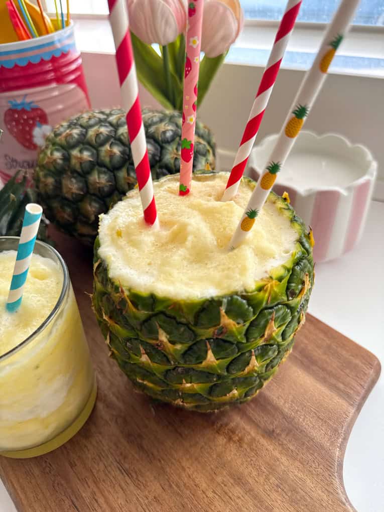 A fresh pineapple filled with slushie with four colourful straws in the top.