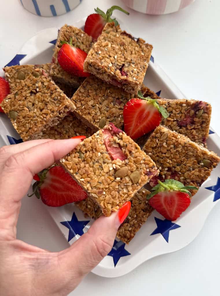 Strawberry oat bars cut into bite size squares and served on a rectangular shaped dish with a bright blue star pattern all over, garnished with fresh strawberries.